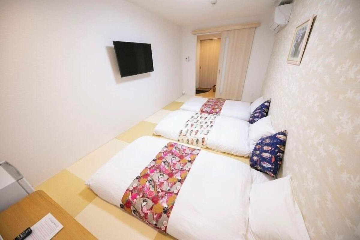 A hotel room with two beds, a flat-screen TV, a wooden desk, and a door leading to a bathroom.