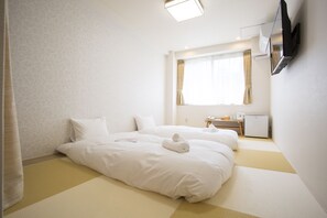 Une chambre d’hôtel avec deux lits, un téléviseur fixé au mur, un petit bureau et une fenêtre avec des rideaux.