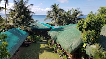 A resort with thatched-roof huts, a paved pathway, and a view of the ocean.
