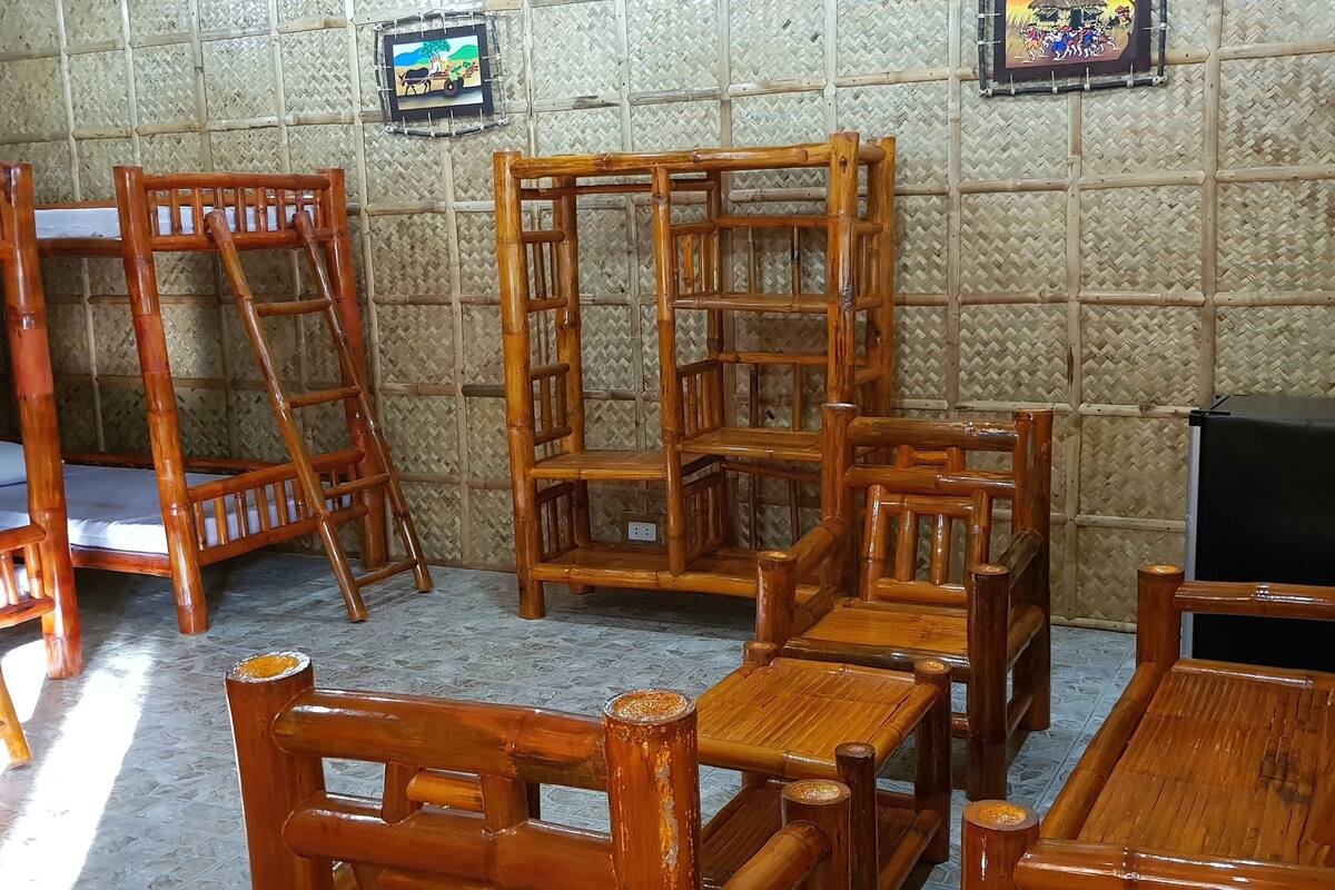 A room with bamboo-patterned walls, multiple wooden furniture pieces including chairs and a table, and a television on a stand.