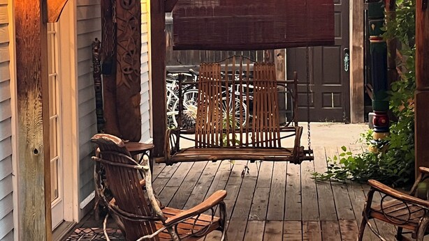 Een rustiek houten terras met een metalen dak, lichtslingers en schommelstoelen.