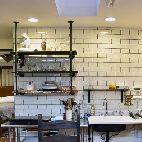 A kitchen with white subway tiles, a black hanging shelf with glassware, a sink with a black faucet, and a yellow lemon on a shelf.