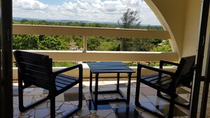 A balcony with a table and two chairs, offering a view of greenery and distant hills. - Alis Plaza (Diani Beach)
