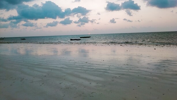 A beach with calm waters, boats, and a cloudy sky. - Alis Plaza (Diani Beach)