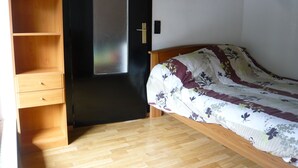 Un dormitorio con cama de madera, armario con estantes múltiples y puerta con panel de vidrio satinado.