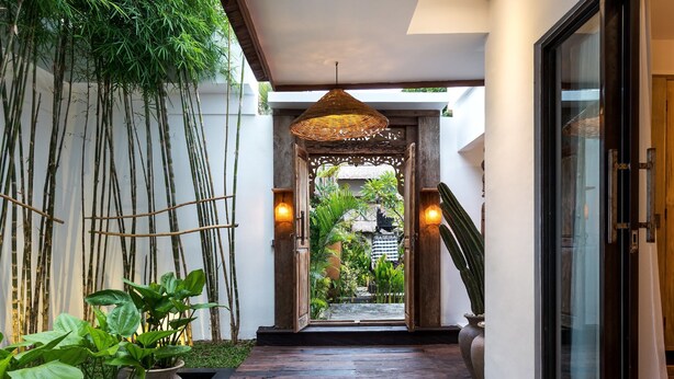 A corridor with a wooden floor, bamboo plants, and a thatched ceiling light. - Villa Metisse by Villa Finder (Seminyak)