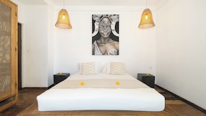 A bedroom with a large bed, two nightstands, a hanging artwork, and two pendant lights.