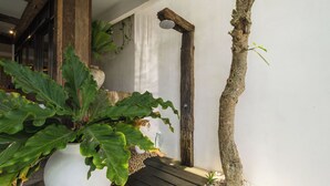 A potted plant with large leaves, a wooden beam, and a small tree trunk against a white wall. - Villa Metisse by Villa Finder (Seminyak)