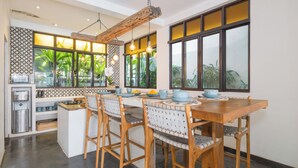 A modern kitchen with a wooden dining table, wicker chairs, and a built-in island. - Villa Metisse by Villa Finder (Seminyak)