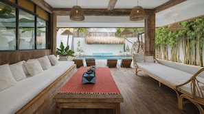 A spacious outdoor lounge area with a wooden table, two sofas, and a pool in the background.