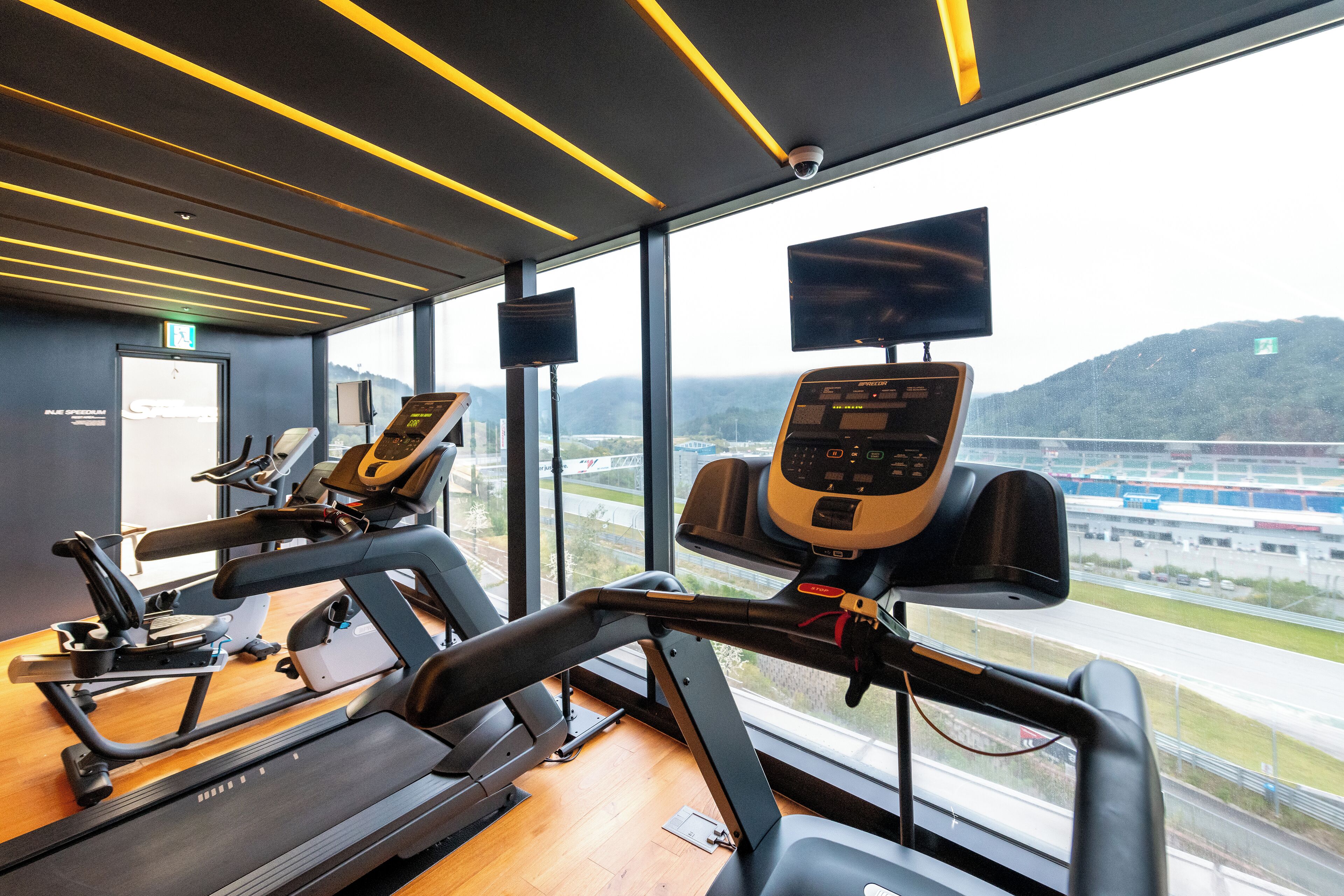 A gym with treadmills and exercise equipment, large windows, and a view of a highway and mountains.