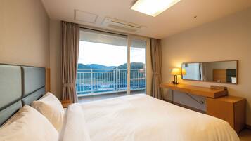 A hotel room with a large bed, a bedside table with a lamp, a mirror, and a view of the mountains through a large window.