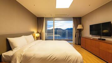 Habitación de hotel con una cama grande, televisión, cómoda de madera y balcón con vista a las montañas.