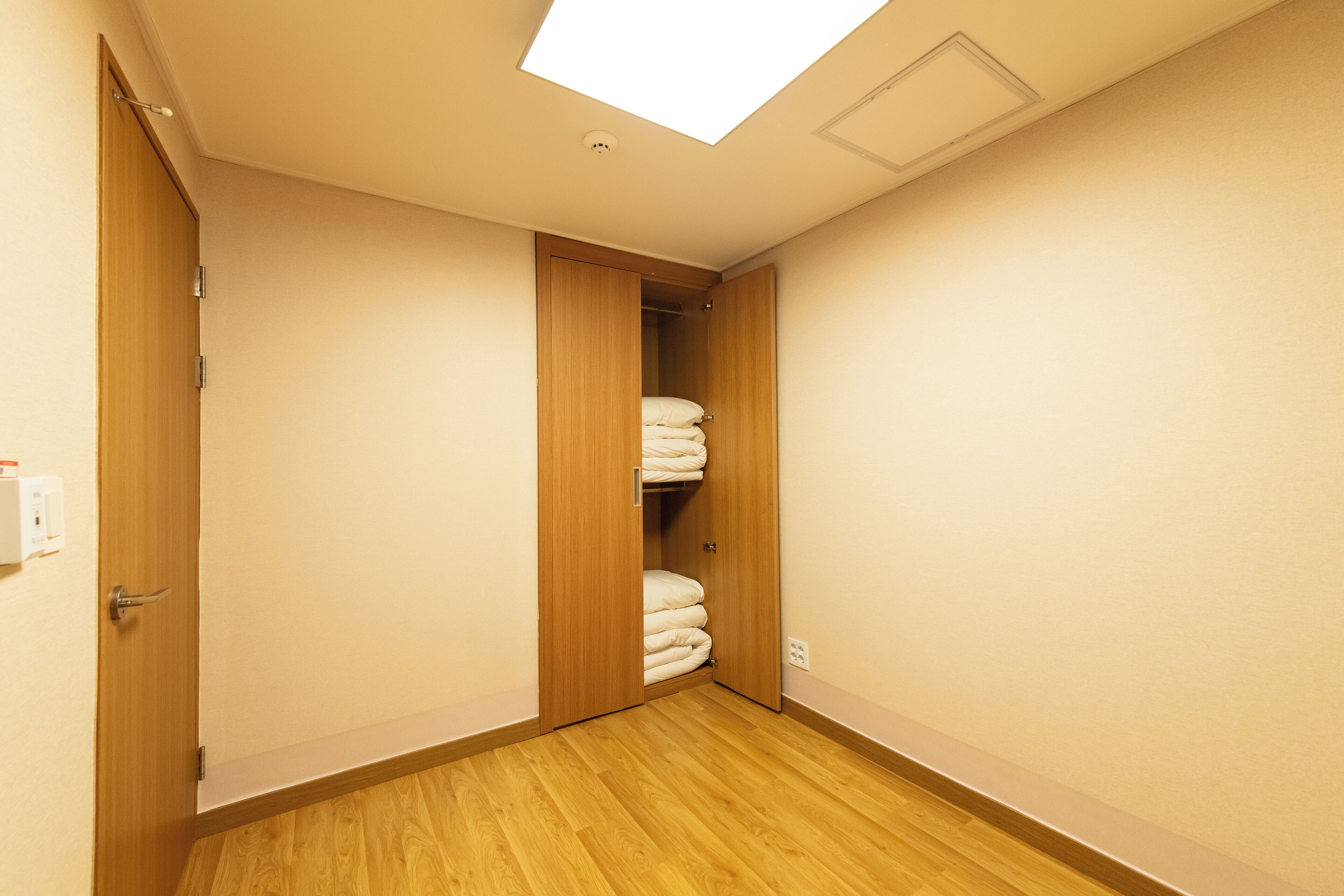 A narrow hallway with wooden flooring, a skylight, and a closet with neatly stacked towels.