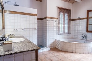 Un bagno con lavandino, doccia e vasca, pareti rivestite di piastrelle e una finestra con persiane.