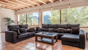 A spacious living area with a large sectional sofa, a glass-top coffee table, and a view of the outdoors through large windows. - Fantastic Villa with Pool, Wi-Fi, Terrace, Garden and Sea View (Sant Josep de sa Talaia)
