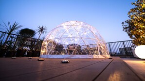 Une structure en forme de dôme géodésique transparente, avec une terrasse en bois à l’avant.