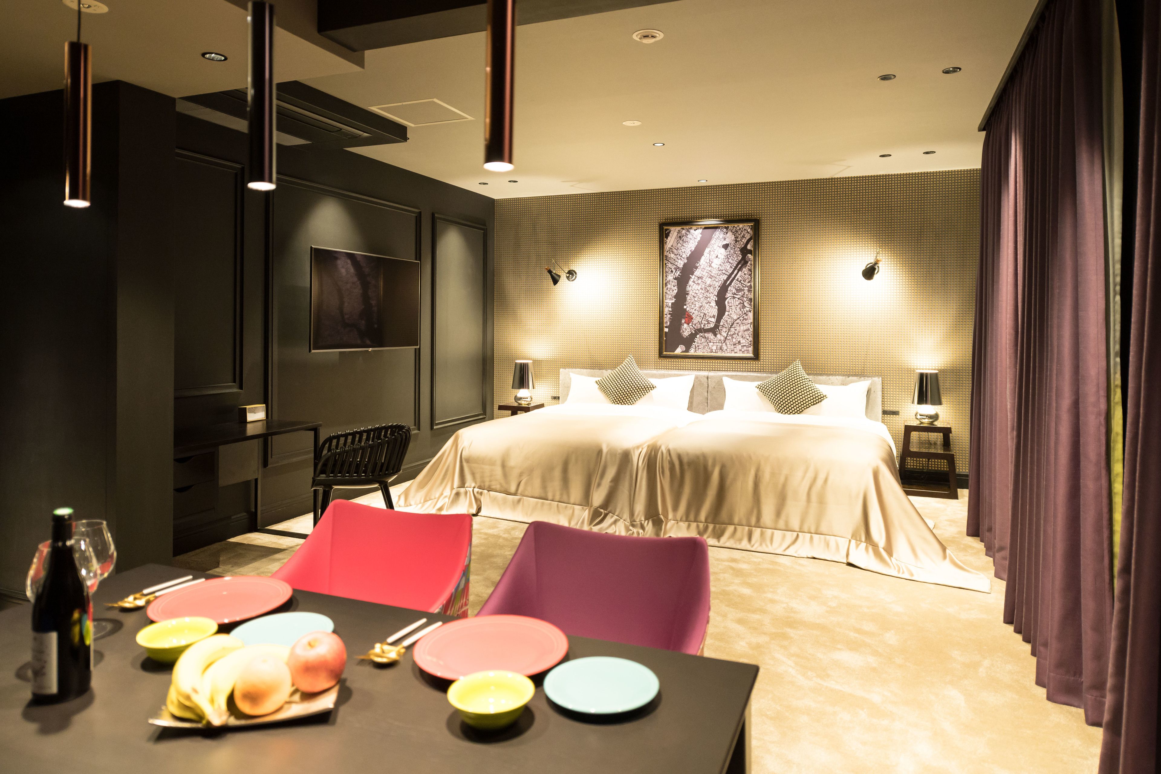 A modern hotel room with a large bed, a dining table with colorful plates, and a bottle of wine.