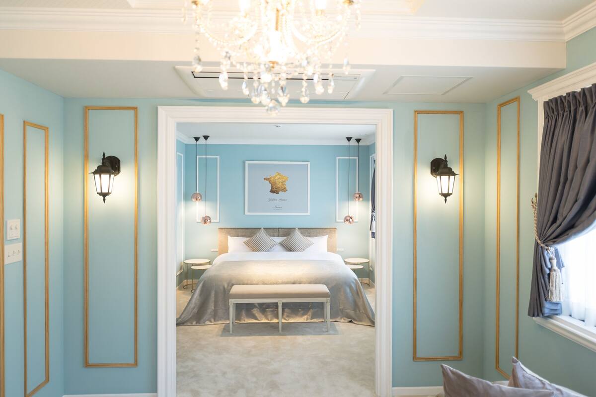 Een slaapkamer met een centraal geplaatst bed, geflankeerd door twee wandlampen, een kroonluchter en een ingelijste foto aan de muur.