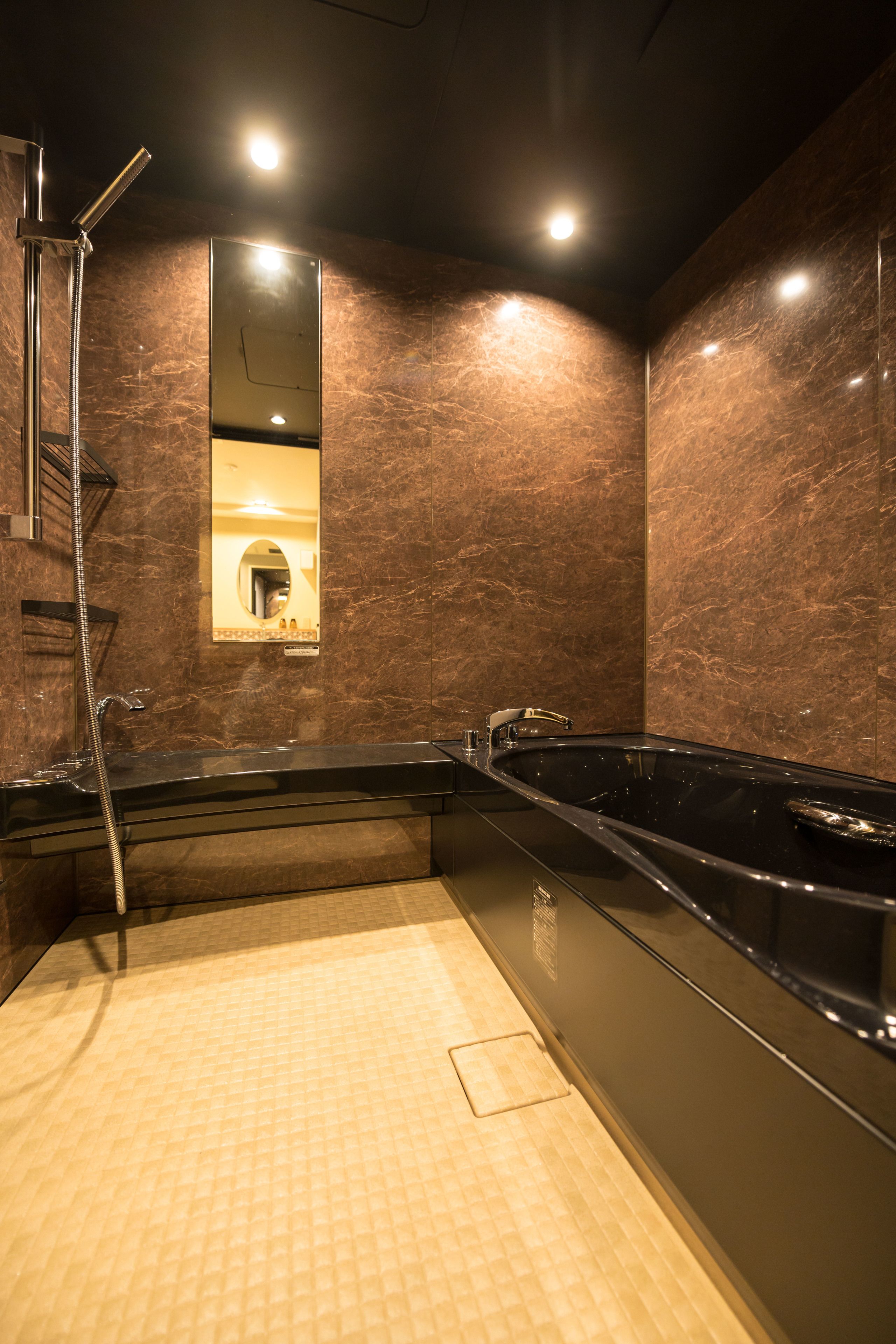 A modern bathroom with a large black bathtub, a shower, and a mirror.