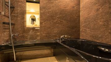 A modern bathroom with a large black bathtub, a shower, and a mirror.