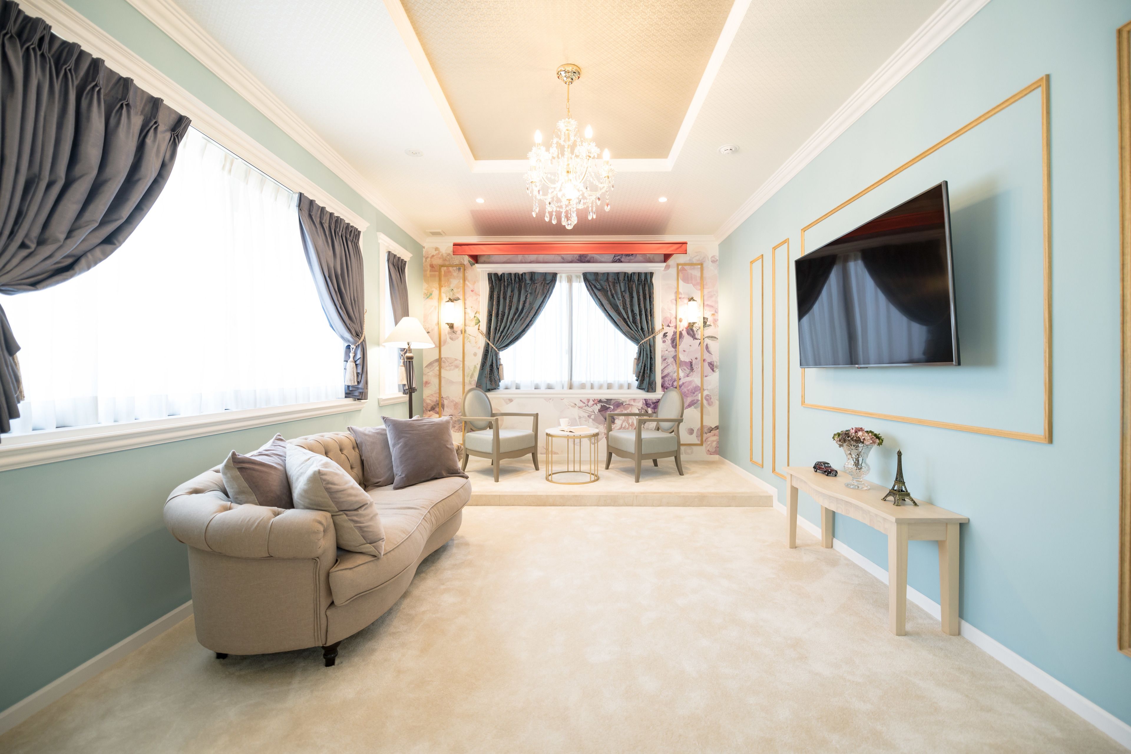 A living room with a beige sofa, two armchairs, a small round table, and a TV mounted on the wall.