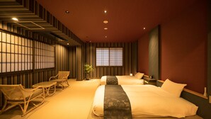 Une chambre d’hôtel avec deux lits, un coin salon avec des fauteuils, une grande fenêtre et un décor mural de style traditionnel.