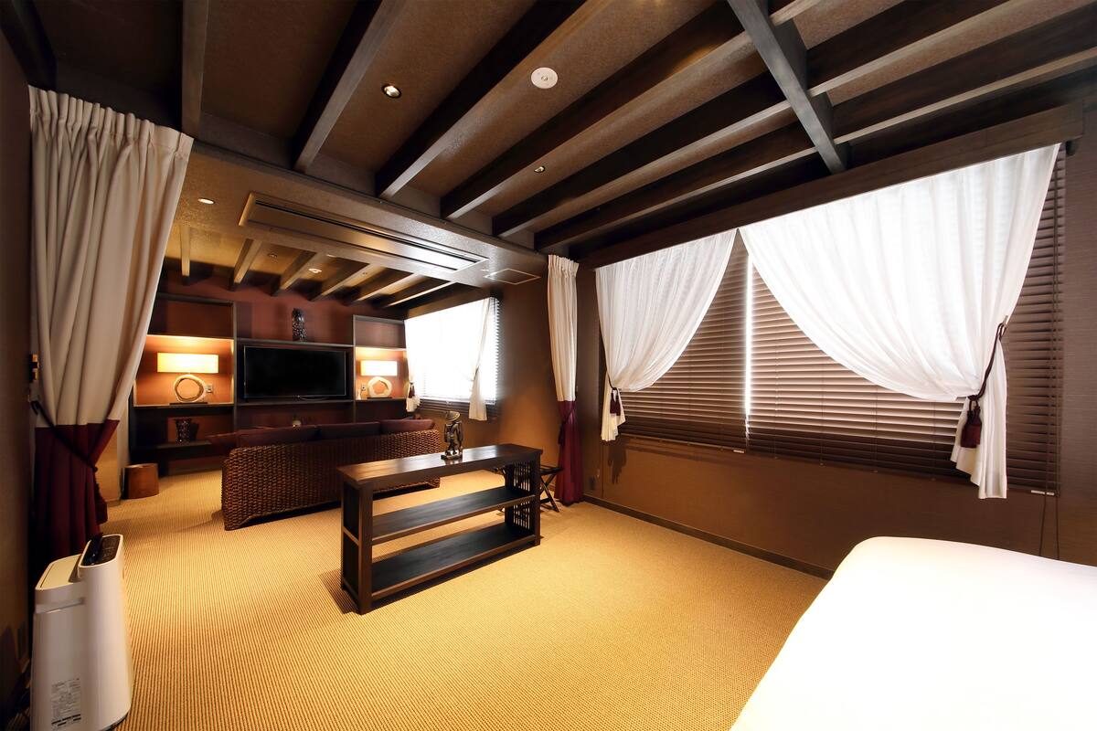 Een hotelkamer met een groot bed, een flatscreen televisie, een zithoek met een bank en een salontafel, en een groot raam met gordijnen.