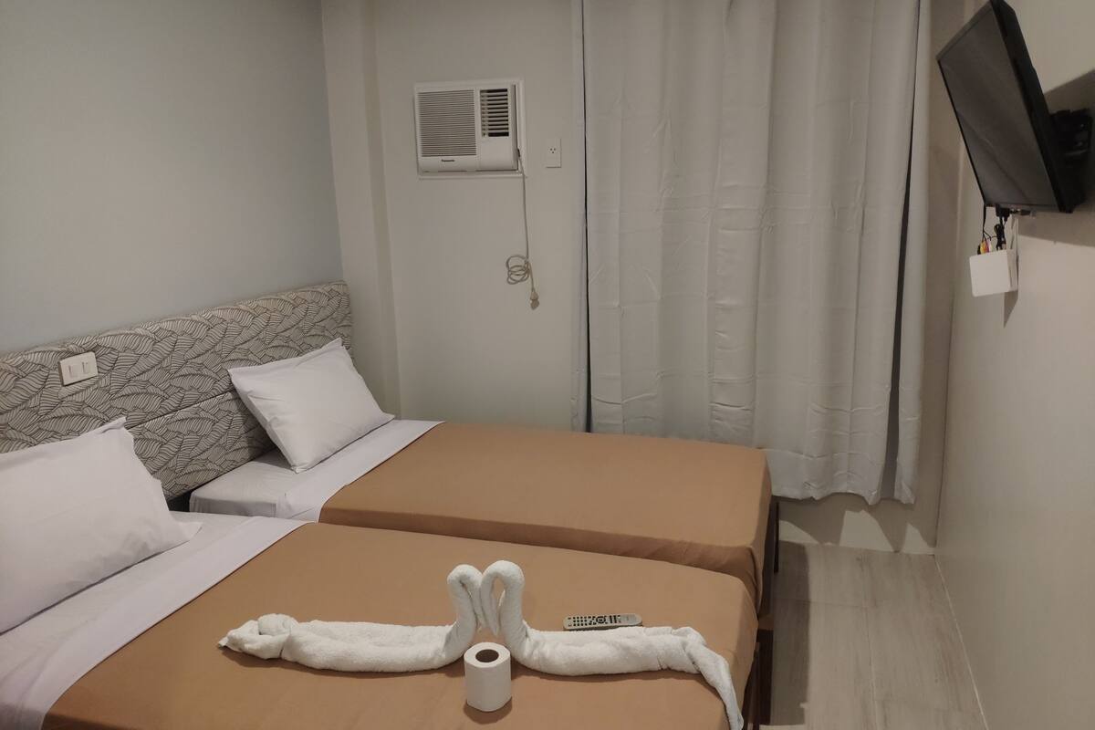 Ein Hotelzimmer mit zwei Betten, einem an der Wand befestigten Fernseher und einem Vorhang.