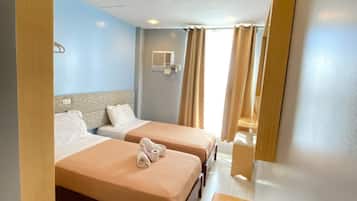 A hotel room with two beds, a wooden nightstand, a bathroom mirror, and a window with curtains.