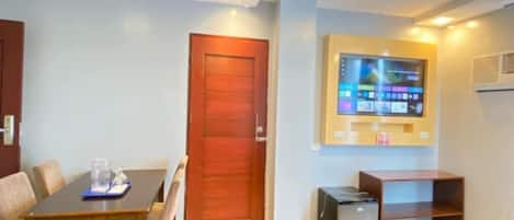 A modern living room with a wooden dining table, a red door, a flat-screen TV mounted on the wall, and a small cabinet.