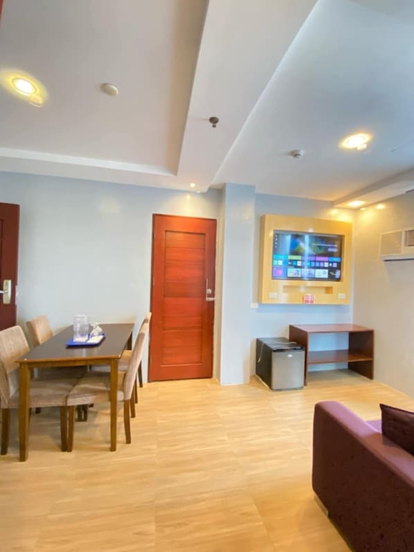 A modern living room with a wooden dining table, a red door, a flat-screen TV mounted on the wall, and a small cabinet. - The Loft Hotel (Iligan)