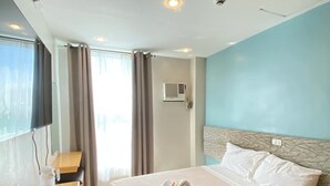 Habitación de hotel con cama, escritorio, silla, ventana con cortinas y aire acondicionado.
