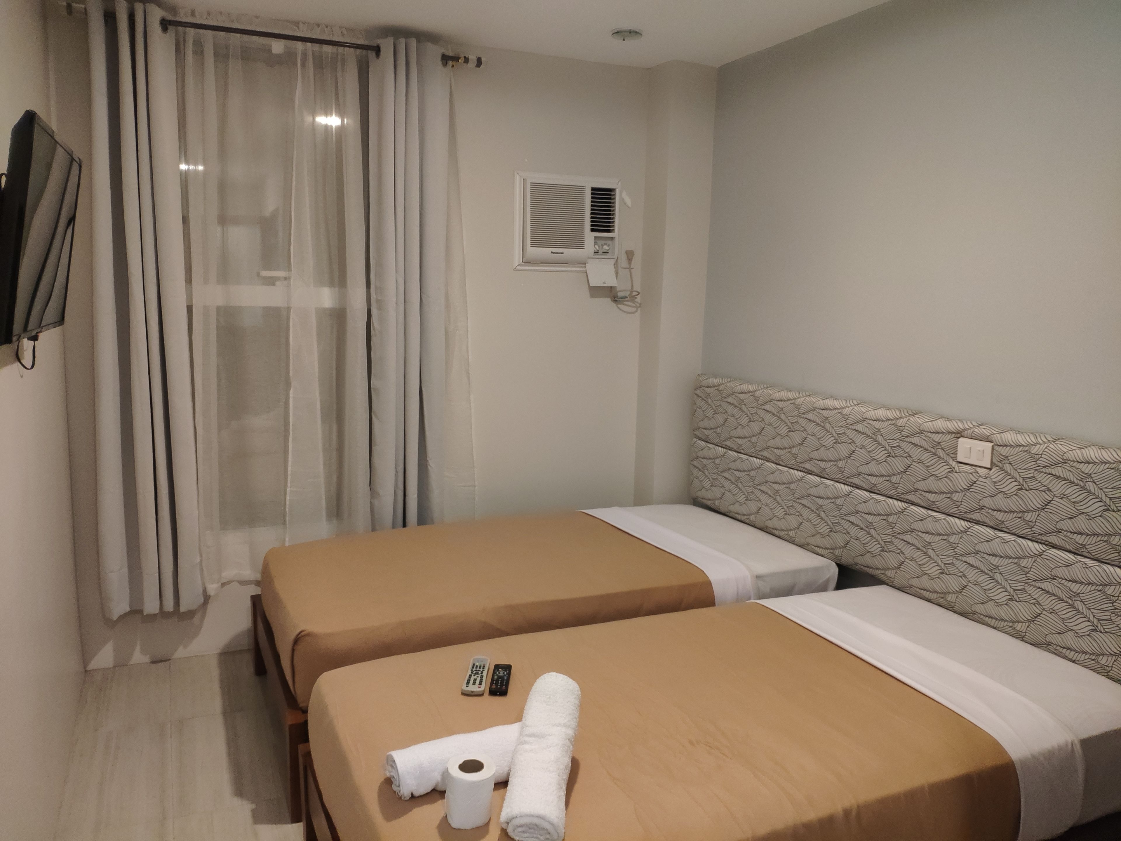 A hotel room with two beds, a shower area, and a wall-mounted air conditioning unit.