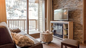 Un salon moderne doté d’un grand téléviseur, d’un plancher en bois, d’un canapé et offrant une vue sur une région montagneuse enneigée.
