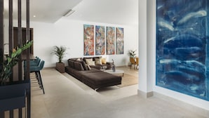 A modern living room with a sectional sofa, a dining area with chairs, and a large abstract painting on the wall.