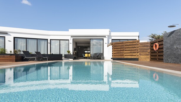 A modern pool area with a clear pool, sun loungers, and a wooden deck.