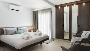 A modern bedroom with a large bed, a walk-in closet, and a seating area.