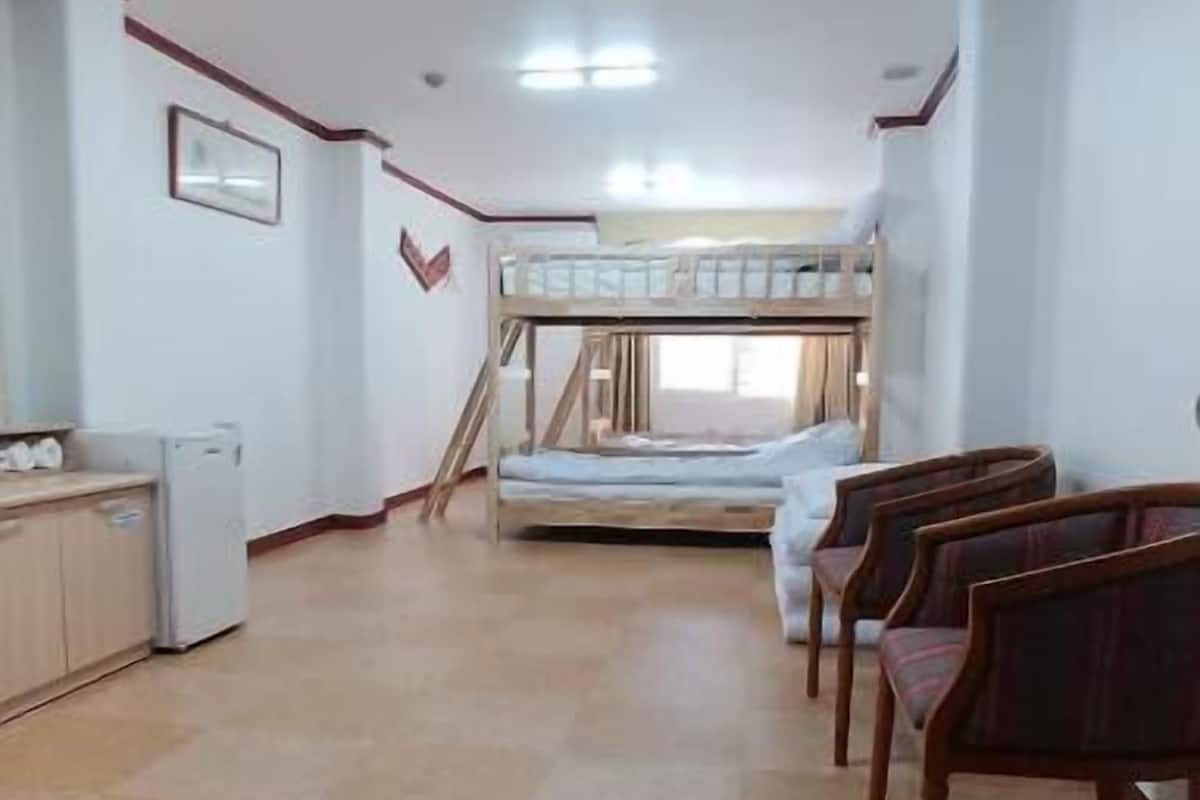 Een kamer met een stapelbed, een klein kitchenette en een rij houten stoelen.