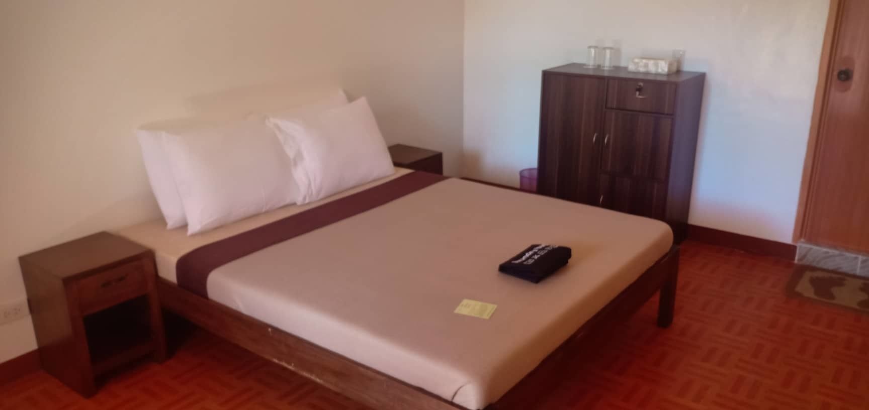A hotel room with a bed, a nightstand, a wardrobe, and a small table.