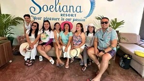 A group of people seated in front of a sign for Soeliana Resort, with a clock and potted plants in the background. - Soeliana Resort (General Luna)