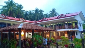 A hotel with a covered outdoor area, palm trees, and a building with a red roof. - Soeliana Resort (General Luna)