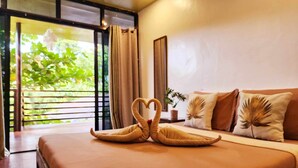 A bedroom with a bed, a sofa, a potted plant, and a view of greenery through a window. - Soeliana Resort (General Luna)