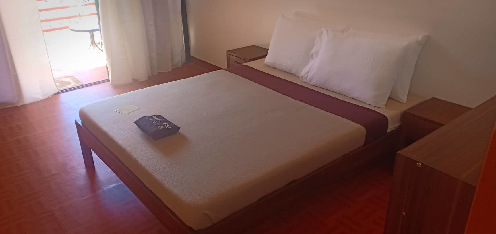 Una cama bien hecha con un cojín y una mesita de noche de madera, un armario ropero de madera.