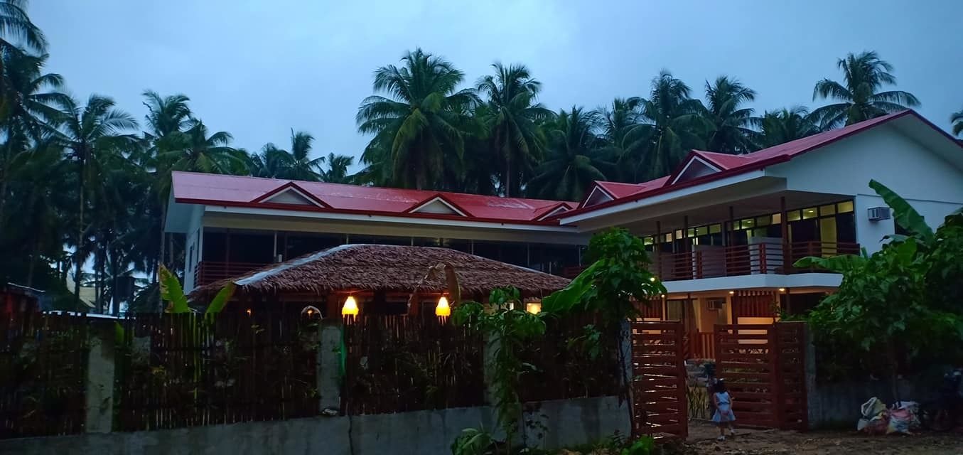 A two-story building with a red roof and a thatched-roof structure.