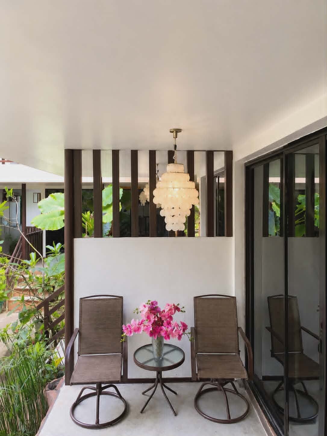 An outdoor seating area with two chairs and a table, a hanging light fixture, and a glass door leading to a garden.