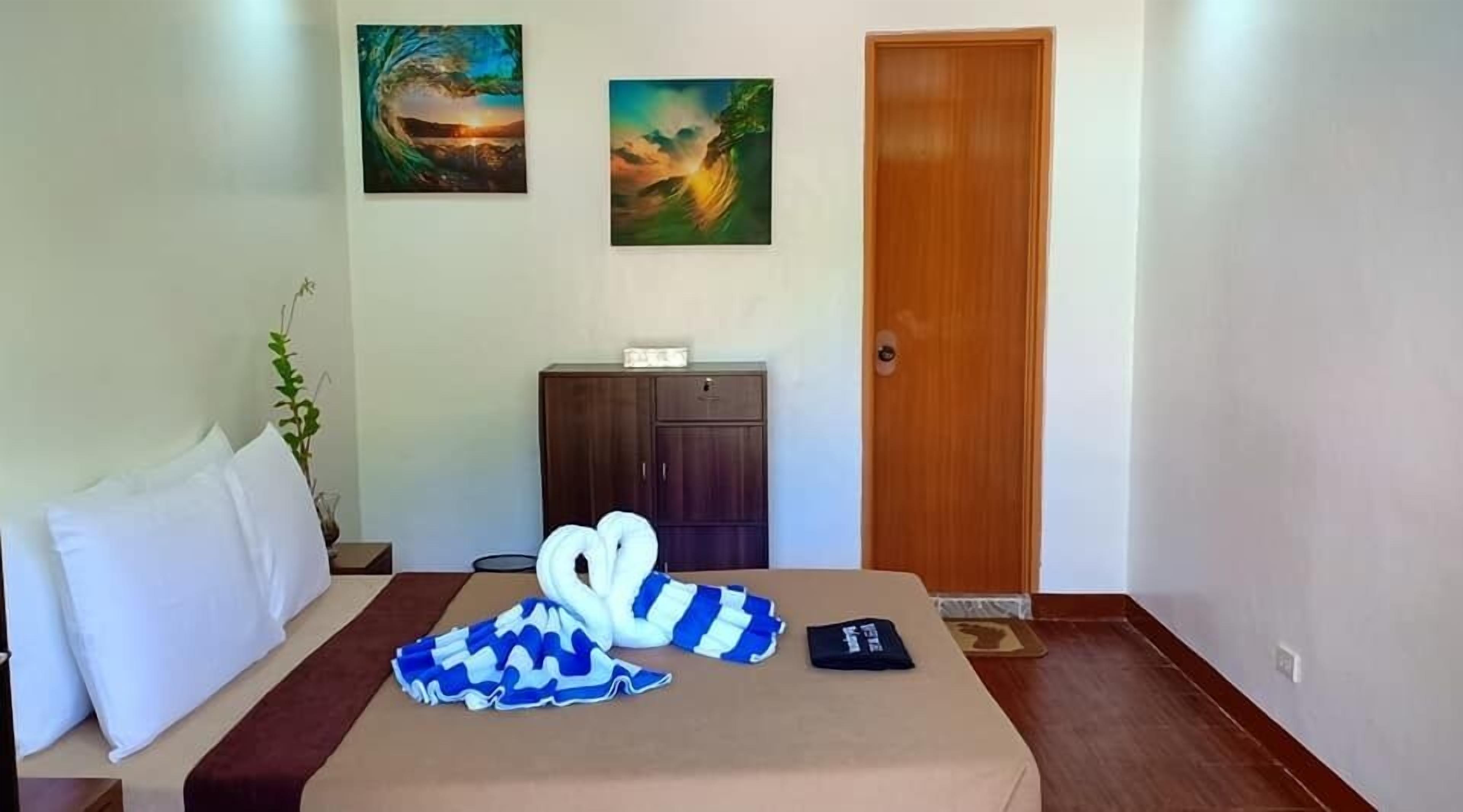 A hotel room with a bed, a wooden wardrobe, and two paintings on the wall.