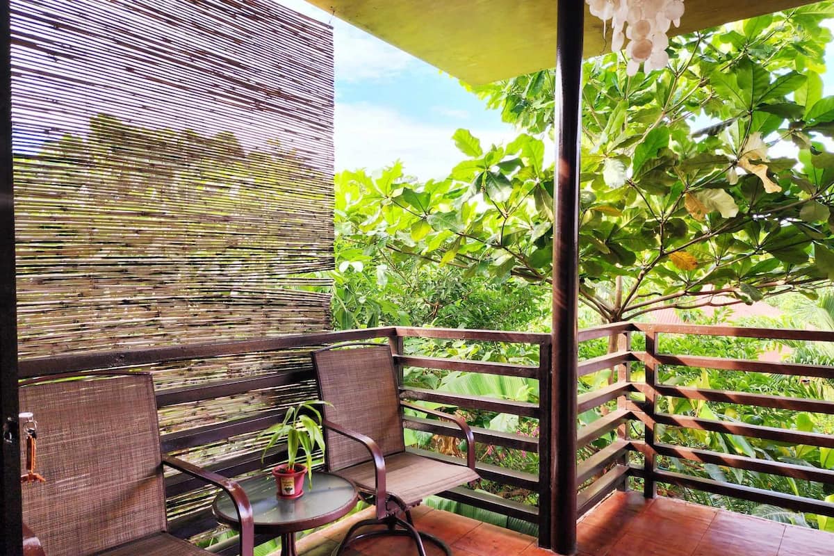 Ein Balkon mit Korbmöbeln, einem kleinen Tisch mit einer Topfpflanze und Blick auf üppiges Grün.