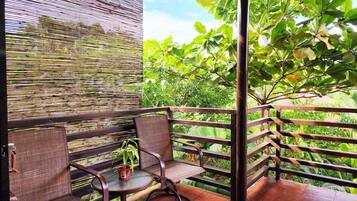 Een balkon met rieten meubels, een kleine tafel met een bloempot, en uitzicht op weelderige begroeiing.