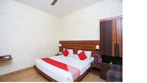 A bedroom with a wooden bed, white walls, a wooden wardrobe, and a plaid chair.